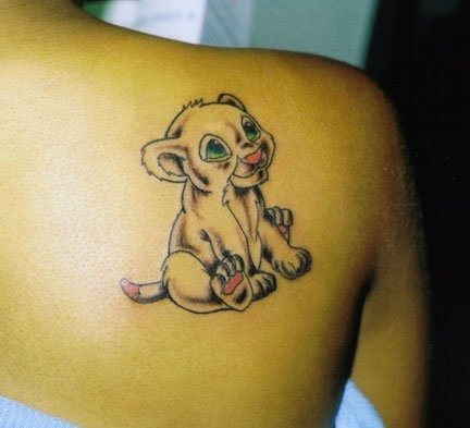 Tatuaje de un cachorro de león sonriente sobre la espalda de esta chica, al tattoo se le han añadido unos ojos de color verde y las palmas de las patas, cola y nariz en color rosa, un diseño muy sencillo que hacen de él un tattoo muy simpático
